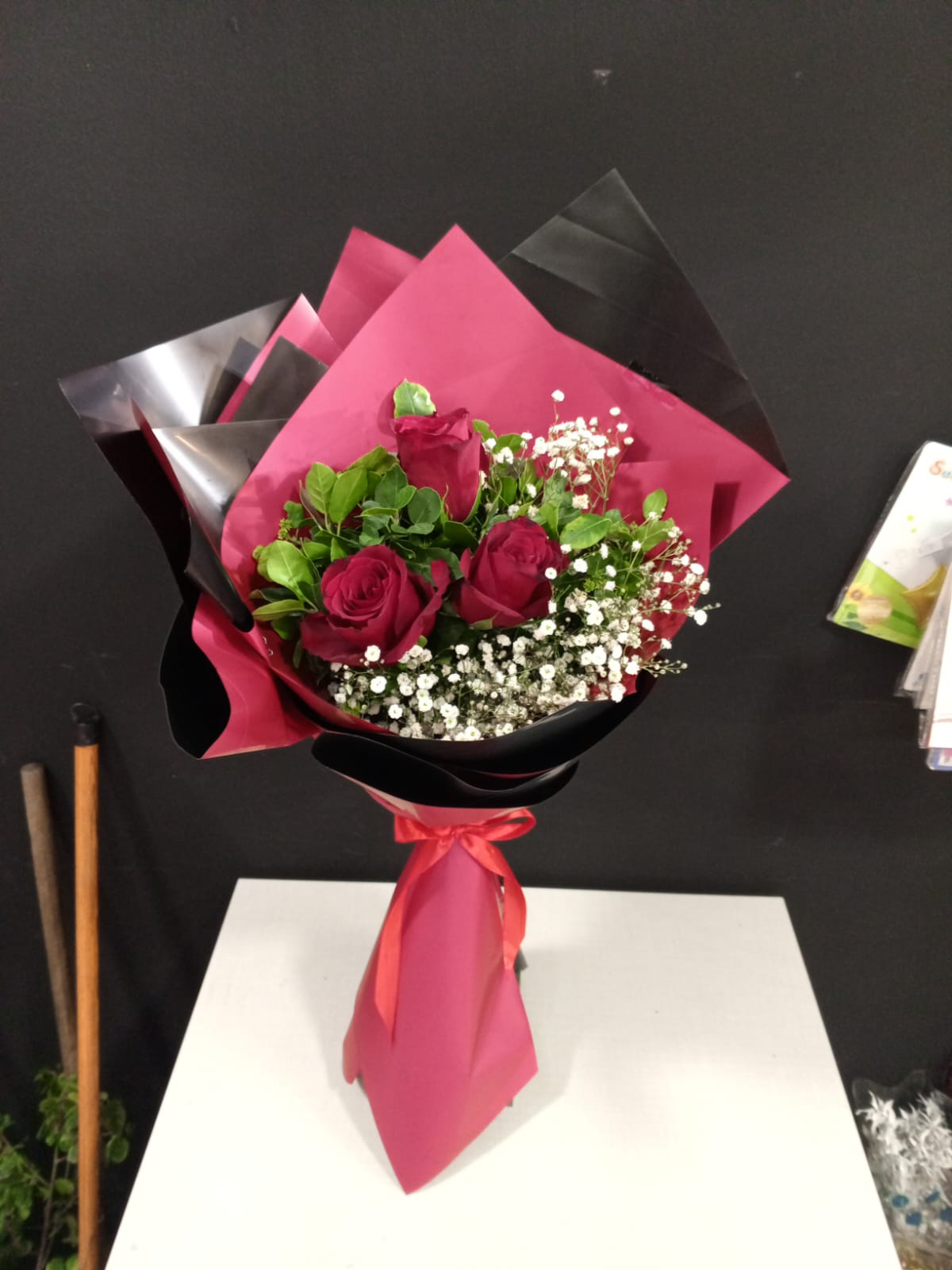 Three red roses with baby's breath in pink and black wrapper with ribbon
